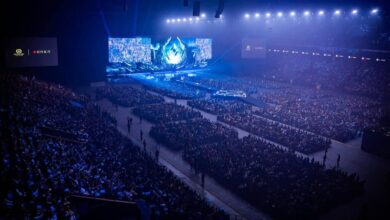 Imagem do palco do evento comunitário Karmine Corp KCX iluminado por luzes azuis. Uma multidão lotada está sentada em frente ao palco
