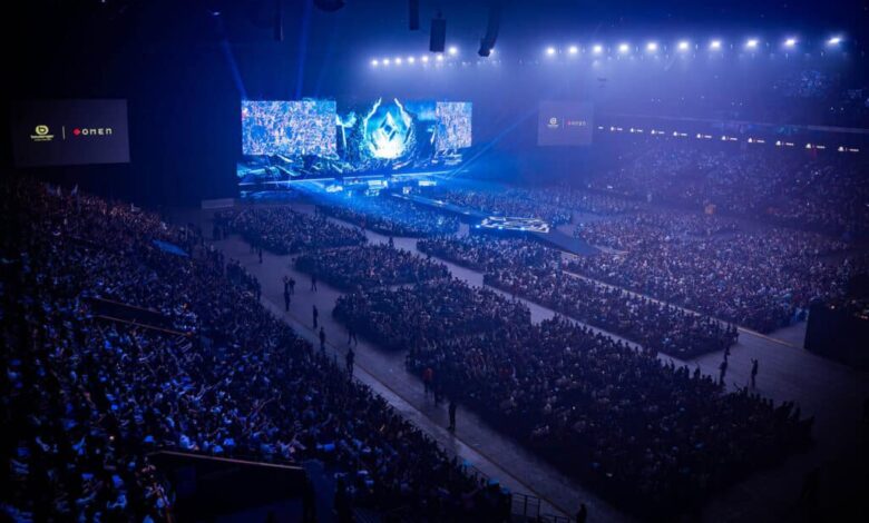 Imagem do palco do evento comunitário Karmine Corp KCX iluminado por luzes azuis. Uma multidão lotada está sentada em frente ao palco