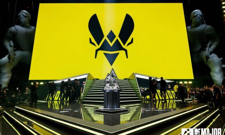 Imagem do logotipo do Team Vitality na tela acima do palco do BLAST Austin Major 2025. O troféu Austin Major está no centro de um palco em uma plataforma